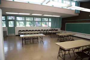 Classroom  with three rectangle tables and a chalkboard on the wall. 