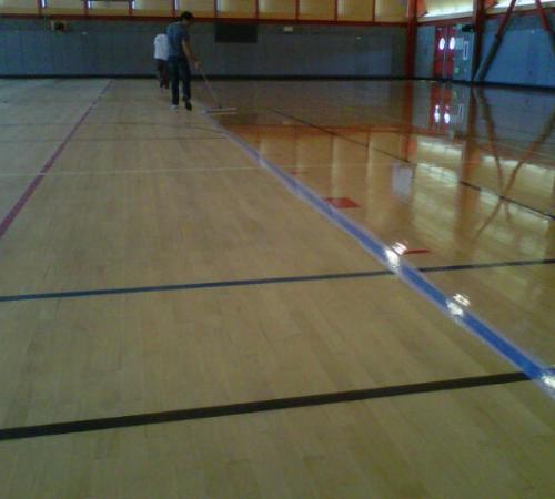 Person applying a first coat to resurface the gym floor.
